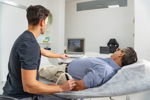 young physiotherapist performs an ultrasound on a patient's arm, both look at the screen at the result